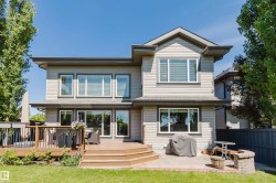 Rear exterior featuring multiple large windows, a two-level wood deck, a patio with brick pavers, and a built-in stone fire pit - 