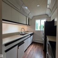 Contemporary kitchen featuring white cabinetry with black trim, a dual basin stainless steel sink, a window, and wood-finish flooring - 
