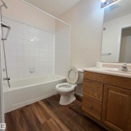 Bathroom with wood-finish flooring, a white bathtub, and white tiled shower surround - 