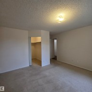 Neutral-toned carpeting spans the room, complemented by light-colored walls and a textured ceiling - 