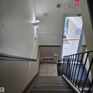 Stairwell entry featuring a metal handrail, wall-mounted sconce lighting, and a tiled floor landing - 