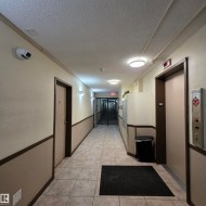 Corridor featuring tile flooring, neutral wall tones with dark trim, recessed ceiling lighting, and an elevator bank with brushed metal controls - 