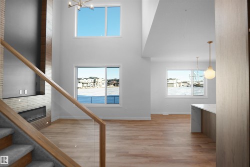 Two-story living room featuring a wood-panel accent wall with built-in media console and linear fireplace, soaring ceilings, and multiple windows - 6403 29 Ave, Edmonton, AB - Indoor Photo Showing Other Room With Fireplace