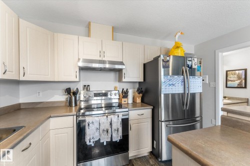 Kitchen featuring light-toned cabinetry, stainless steel appliances, and wood-finish flooring - 2324 30 Avenue, Edmonton, AB 