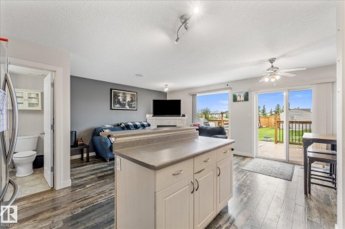 Open-concept living space featuring wood-finish flooring, a kitchen island with storage, and sliding glass doors leading to a wooden deck - 2324 30 Avenue, Edmonton, AB 