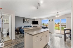 Open-concept living space featuring wood-finish flooring, a kitchen island with storage, and sliding glass doors leading to a wooden deck - 