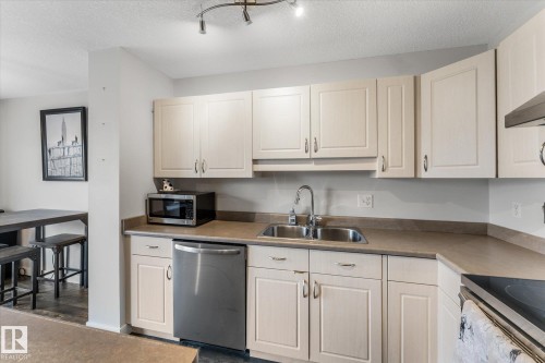 Kitchen featuring light-toned cabinetry with curved hardware, a double-basin stainless steel sink with a gooseneck faucet, and a stainless steel dishwasher - 2324 30 Avenue, Edmonton, AB 