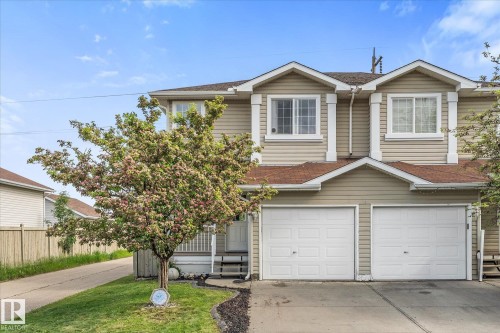 Two-story duplex featuring neutral-toned siding, a double garage with white panel doors, and a front yard with a blooming tree - 2324 30 Avenue, Edmonton, AB 