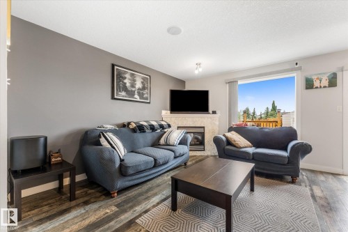 Living area featuring wood-finish flooring, a fireplace with a light-toned surround, a window offering exterior views, and a ceiling-mounted light fixture - 2324 30 Avenue, Edmonton, AB 