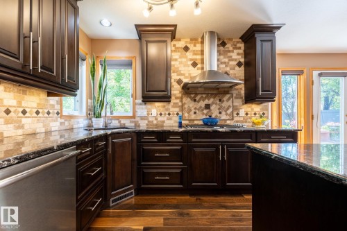 Kitchen featuring dark wood cabinetry, stainless steel appliances, granite countertops, and a patterned tile backsplash - 315 Osland Place, Edmonton, AB 