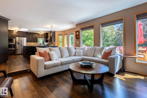 Open-concept living area featuring rich wood-finish flooring, abundant natural light from multiple windows, recessed lighting, a modern kitchen with dark cabinetry, and stainless steel appliances - 315 Osland Place, Edmonton, AB 