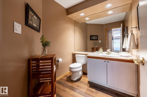 Contemporary bathroom featuring wood-finish flooring, a white vanity with a light-colored countertop, an integrated sink, and an expansive wall mirror with recessed lighting - 315 Osland Place, Edmonton, AB 