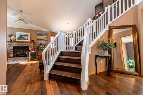Grand entryway featuring wood-finish flooring, a curved staircase with white balusters, and a living area with a stone-surround fireplace - 315 Osland Place, Edmonton, AB 