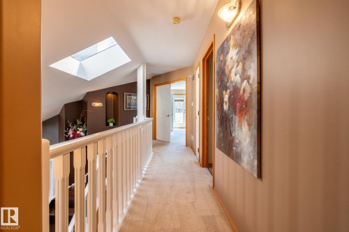 Hallway featuring light-toned carpeting, a white spindle railing, and a skylight - 315 Osland Place, Edmonton, AB 