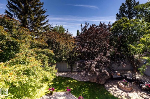 Landscaped backyard featuring a paver patio with seating, fire pit, and mature trees - 315 Osland Place, Edmonton, AB 