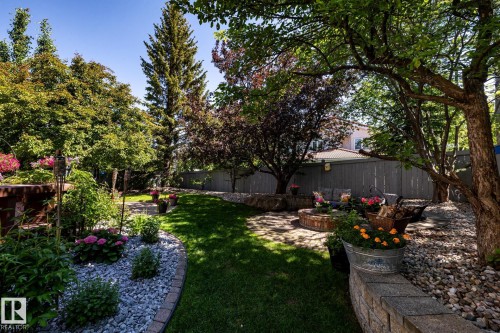 Expansive backyard featuring a manicured lawn, established trees, a stone patio, a built-in fire pit, and a retaining wall with stone veneer - 315 Osland Place, Edmonton, AB 