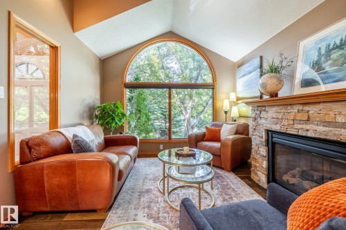 Living area featuring a floor-to-ceiling arched window, a stone-clad fireplace, vaulted ceilings, and wood-finish flooring - 315 Osland Place, Edmonton, AB 
