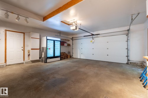 Spacious garage with a concrete floor, exposed wood ceiling beams, and a white paneled garage door - 315 Osland Place, Edmonton, AB 