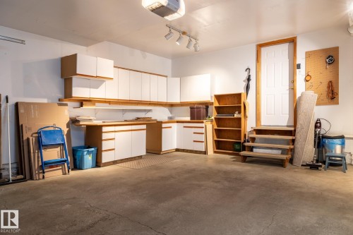 Spacious garage featuring extensive built-in cabinetry with wood-finish accents, a dedicated workbench area, and a utility door with a wooden staircase - 315 Osland Place, Edmonton, AB 