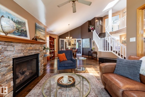 Living area featuring a stone-clad fireplace with a wood mantel, wood-finish flooring, and a white open-railing staircase - 315 Osland Place, Edmonton, AB 