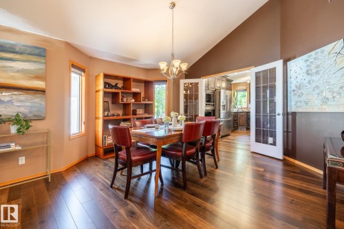 Spacious dining area featuring rich wood-finish flooring, a contemporary chandelier, built-in shelving, ample natural light from multiple windows, and French doors opening to an adjacent kitchen space - 315 Osland Place, Edmonton, AB 