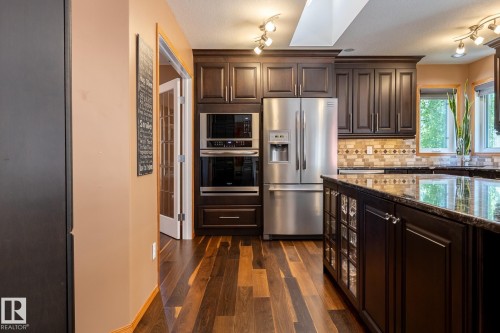 Kitchen featuring rich wood-finish flooring, dark wood cabinetry, stainless steel appliances including a double oven and French door refrigerator, and a kitchen island with a polished countertop - 315 Osland Place, Edmonton, AB 