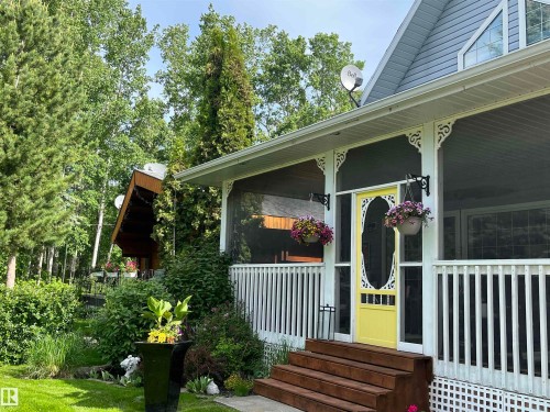 Screened-in front porch featuring a decorative yellow storm door, white balustrade railing, and ornate corbel details - B13 Johnsonia Beach, Rural Leduc County, AB 