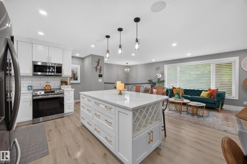 Open-concept living area featuring a large kitchen island with built-in wine storage, white cabinetry with gold hardware, stainless steel appliances, and recessed lighting - 43 Burnham Place, St. Albert, AB 