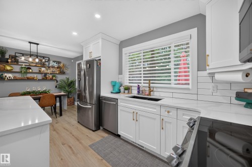 Modern kitchen featuring white cabinetry with gold-tone hardware, wood-finish flooring, stainless steel appliances, a white subway tile backsplash, and light-toned countertops - 43 Burnham Place, St. Albert, AB 