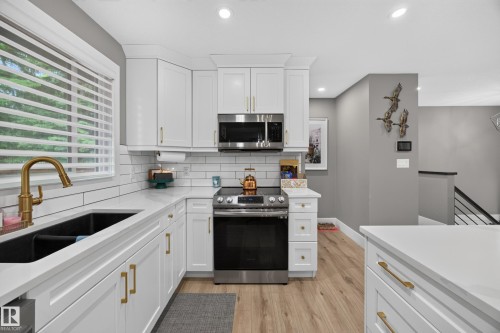 Modern kitchen with white cabinetry, stainless steel appliances, and a black double-basin sink with a brass faucet - 43 Burnham Place, St. Albert, AB 