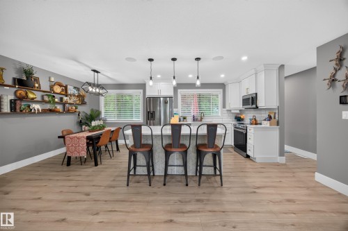 Open-concept kitchen and dining area featuring light wood-finish flooring, white cabinetry, a central island with pendant lighting, and stainless steel appliances - 43 Burnham Place, St. Albert, AB 