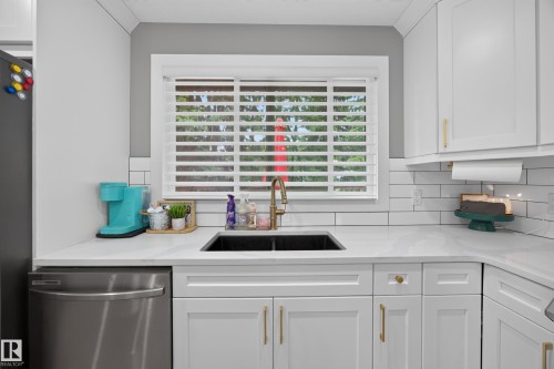 Kitchen featuring white shaker-style cabinetry with gold-toned hardware, solid surface countertops, and a white subway tile backsplash - 43 Burnham Place, St. Albert, AB 