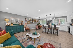 Open-concept living space featuring wood-finish flooring, recessed lighting, and a white kitchen with an island and pendant lights - 