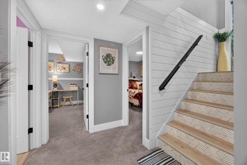 Staircase featuring wood-finish treads with patterned risers, a black metal handrail, and white shiplap-style wall paneling - 43 Burnham Place, St. Albert, AB 