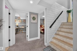 Staircase featuring wood-finish treads with patterned risers, a black metal handrail, and white shiplap-style wall paneling - 