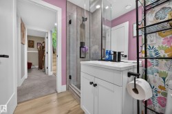 Bathroom featuring a glass-enclosed shower with tile surround, a white vanity with integrated sink and black faucet, and wood-finish flooring - 