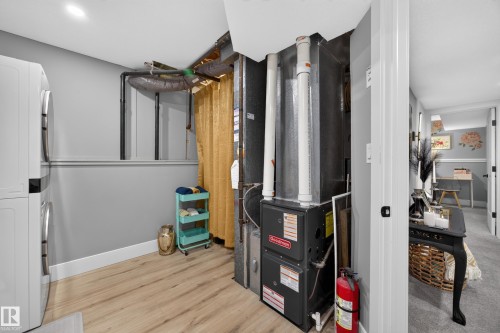 Utility space featuring wood-finish flooring, a stacked washer and dryer, and a Goodman furnace system - 43 Burnham Place, St. Albert, AB 