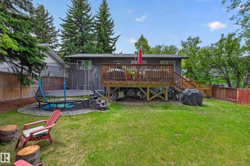 Expansive backyard featuring a manicured lawn, a raised wooden deck with railings, and mature evergreen trees providing natural screening - 43 Burnham Place, St. Albert, AB 