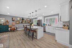 Open concept kitchen featuring white cabinetry, stainless steel appliances, a center island with pendant lighting, and wood-finish flooring - 
