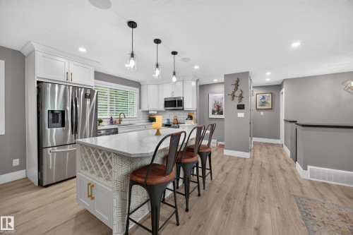 Open-concept kitchen featuring white shaker cabinetry, stainless steel appliances, and a central island with integrated wine storage - 43 Burnham Place, St. Albert, AB 