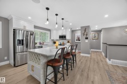 Open-concept kitchen featuring white shaker cabinetry, stainless steel appliances, and a central island with integrated wine storage - 