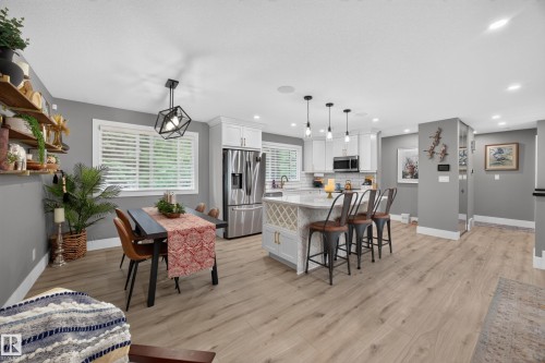 Open-concept kitchen and dining area featuring wood-finish flooring, white cabinetry, stainless steel appliances, and a kitchen island with built-in wine storage - 43 Burnham Place, St. Albert, AB 