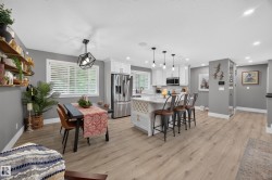 Open-concept kitchen and dining area featuring wood-finish flooring, white cabinetry, stainless steel appliances, and a kitchen island with built-in wine storage - 
