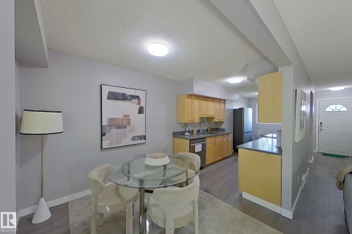 Open-concept living area featuring a glass-top dining table, light wood cabinetry, gray countertops, and wood-finish flooring - 176 Centennial Court, Edmonton, AB 