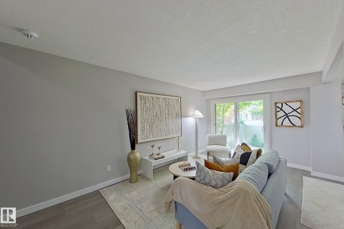 Spacious living area featuring light gray walls, wood-finish flooring, white baseboards, and a sliding glass door providing natural light - 176 Centennial Court, Edmonton, AB 