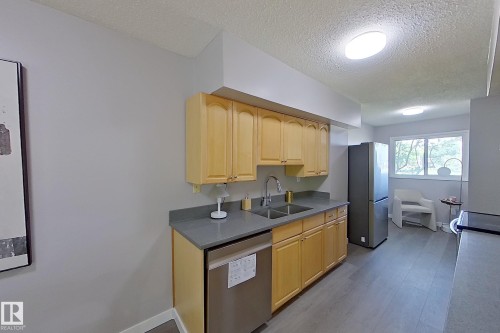 Kitchen featuring light wood cabinetry, gray countertops, a stainless steel double-basin sink with a gooseneck faucet, and stainless steel appliances, including a dishwasher and refrigerator - 176 Centennial Court, Edmonton, AB 