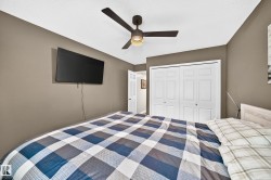 Bedroom featuring a dark-toned ceiling fan with integrated lighting, a wall-mounted display, and a built-in closet with bi-fold paneled doors - 