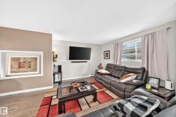 Living area with wood-finish flooring, light grey and tan walls, and a window with blinds - 