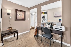 Open concept space featuring light wood-finish flooring, a wall-mounted sconce, and a pass-through window overlooking a dedicated laundry area with stacked appliances - 