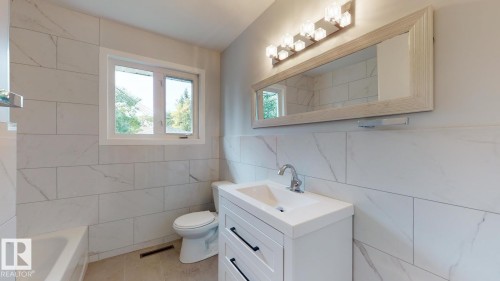 Bathroom featuring white subway tile walls, a built-in bathtub, a window, a white vanity with an integrated sink, and a framed mirror with overhead lighting - 11744 135 Street, Edmonton, AB - Indoor Photo Showing Bathroom